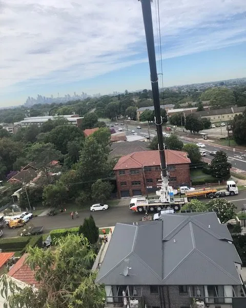 Aerial view of a crane working between apartment buildings with the city skyline behind